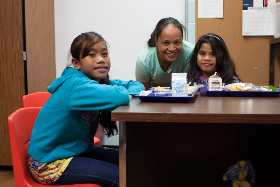 Two young girls and woman look at the camera with lunch trays in front of them
